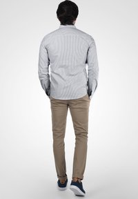 Lys blå og hvit stripete skjorte med lange ermer, tan slim-fit bukser og blå joggesko, sett bakfra.
