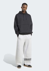 Svart huva sweatshirt med en framlapp, kombinerad med grå vida sweatpants med svarta randiga detaljer vid mudden. Svarta sneakers.