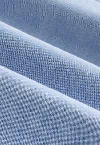 Hellblaue, strukturierte Stoff mit dichter Webart, der kleine gleichmäßige Punkte zeigt. Die Oberfläche ist glatt und leicht reflektierend.