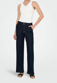 Mörka denimvid byxor med knäppning fram och sidofickor. Parat med en figurnära vit ärmlös topp.