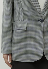 Een geruite blazer met blauwe, zwarte en witte patronen, voorzien van een enkele knoopsluiting en een voorkennis, gemaakt van textiel met een structuur.