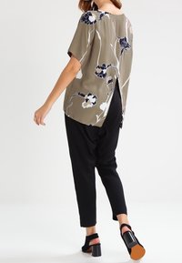 Olivengrøn bluse med hvidt og marineblåt blomsterprint, korte ærmer og åben ryg, parret med sorte tapered bukser og blokhælede sandaler.