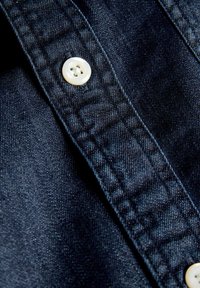 Tissu en denim bleu foncé avec un gros plan sur une couture cousue et deux boutons en plastique blanc cousus sur le tissu.