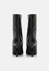 Svarte lær ankelstøvler med et elegant design, spiss tå og blanke stiletthæler. Bakre glidelås og glatt tekstur.