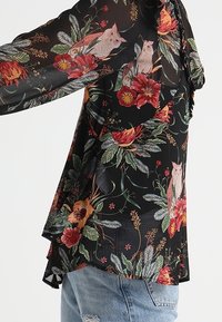 Zwarte bloemenblouse van sheer stof, met kleurige bloemen- en uilenpatronen, lange mouwen en een uitlopende zoom.