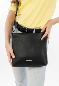 Borsa a tracolla in pelle nera con una texture a granuli, forma rettangolare, accento con logo argentato e tracolla regolabile.