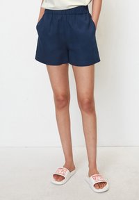 Námořnické modré, lehké šortky s elastickým pasem, bočními kapsami a uvolněným střihem; v kombinaci s bílými klouzavými sandály s červeným nápisem.