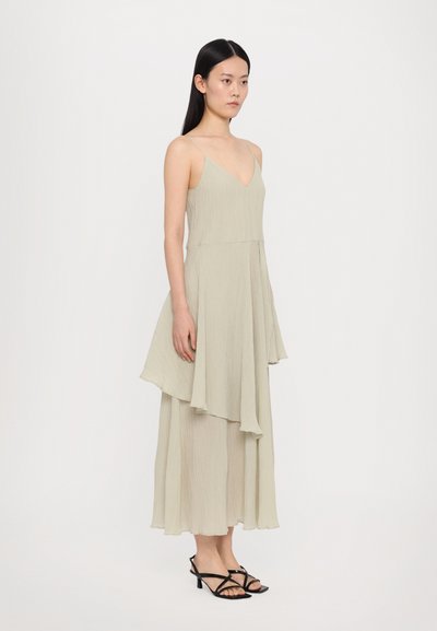 Light green, pleated maxi dress with a V-neck, asymmetrical hem, and thin straps. Worn with black strappy heels.