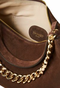 Interno di una borsa a tracolla in suede marrone con una zip dorata. Presenta una tracolla in catena dorata e un'etichetta con testo impresso che legge "TWINSSET MILANO."