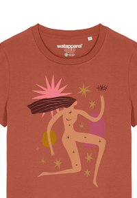 T-shirt de couleur rouille avec un design graphique représentant une figure féminine stylisée, des étoiles et des formes abstraites en rose, jaune et vert.