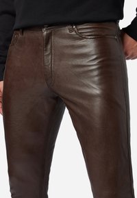 Bruine leren broek met een slim fit-ontwerp, een gladde textuur en zichtbare stikdetails bij de zakken en de tailleband.