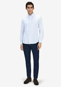 Vaaleansininen ja valkoinen raidallinen nappipaita pitkillä hihoilla, yhdistettynä tummansiniteisiin housuihin ja ruskeisiin kenkiin. Sisältää klassisen kauluksen muotoilun.