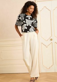 Blusa nera a fiori con maniche corte, abbinata a pantaloni a gamba larga beige chiaro, con una vestibilità comoda e tasche laterali.