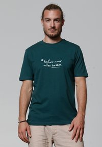 Teal katoenen t-shirt met korte mouwen en ronde halslijn. Voorzien van witte tekst die zegt "Früher war alles besser." op de voorkant.