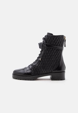 Bottine noire en cuir avec panneaux latéraux matelassés, lacets à l'avant, sangle latérale, fermeture éclair à l'arrière et semelle épaisse en caoutchouc avec petit talon.