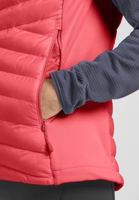 Gilet rosso imbottito in tessuto sintetico, con pannelli a sacco orizzontali, tasca laterale con zip e una foderatura a maniche lunghe di colore blu navy.