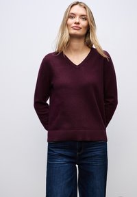 Burgundy stickad tröja med V-ringning, långa ärmar och ribbad nederkant. I kombination med mörkblå denimjeans. Slät textur.