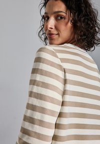 Suéter a rayas en tonos beige y crema con un cuello redondo y un borde acanalado. Textura suave y corte relajado, visto desde un ángulo de tres cuartos.
