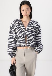 Top cropped às riscas zebra preto e branco com mangas bufantes, cintura ajustada e detalhe de laço no decote, combinado com calças bege.