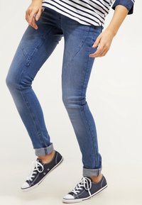 Jeans de denim azul con un corte slim, que presentan una pierna ajustada, detalles de costura sutiles y un dobladillo con vuelta, combinados con zapatillas de lona navy.
