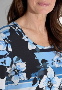 Bloemtop met blauwe en zwarte kleuren, ronde halslijn, korte mouwen en een patroon van grote bloemen met blauwe accenten en strepen.