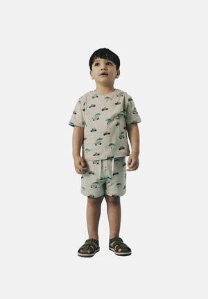 Camicia beige a maniche corte e pantaloni corti con un motivo di veicoli e alberi, abbinati a sandali marroni. Tessuto morbido, vestibilità rilassata, design informale.