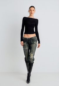 Bluză neagră cu mâneci lungi și design pe umeri, combinată cu blugi din denim robust, cu accente cu ținte și rupturi la genunchi; cizme negre până la genunchi.