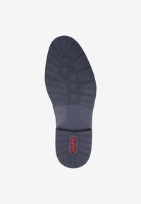 Suola di una scarpa realizzata in gomma nera flessibile, con un motivo testurizzato per la presa e un logo rosso prominente al centro.