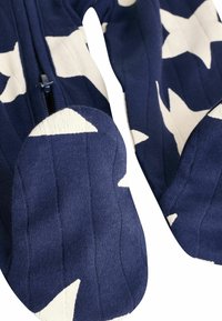 Gros plan sur un tissu en maille bleu marine avec des motifs d’étoiles blanches et un détail de fermeture éclair sur un vêtement.