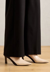 Talons aiguilles beiges et noirs au design épuré, présentant un bloc de couleur contrastant et un petit talon robuste.