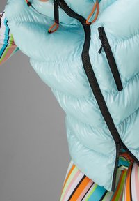 Světlomodrá péřová vesta s lesklým povrchem, černými zipy a oranžovými šňůrkami. Horizontální prošívaný vzor.