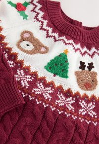 Pull de Noël avec des motifs bordeaux, blancs et orange, présentant des motifs tricotés d’un ours, d’un sapin, de rennes et de feuilles de houx.