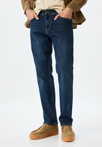 Jeans de denim azul oscuro con un corte clásico de pierna recta, que cuentan con bolsillos frontales, cremallera y una sutil textura desgastada.