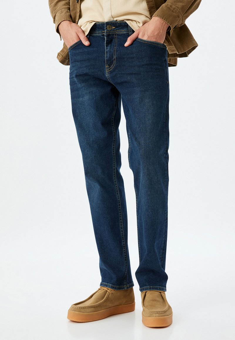 Jeans de denim azul oscuro con un corte clásico de pierna recta, que cuentan con bolsillos frontales, cremallera y una sutil textura desgastada.