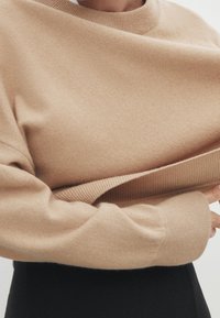 Beige oversized tröja med rund halsringning och ribbade ärmslut. Mjuk textur, med en vikt nederkant som ger en djupare dimension till designen.