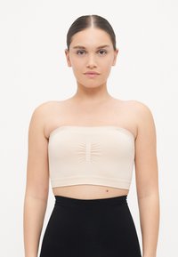Beige strapless bandeau top made of smooth fabric with a center ruching detail, paired with high-waisted black bottoms.