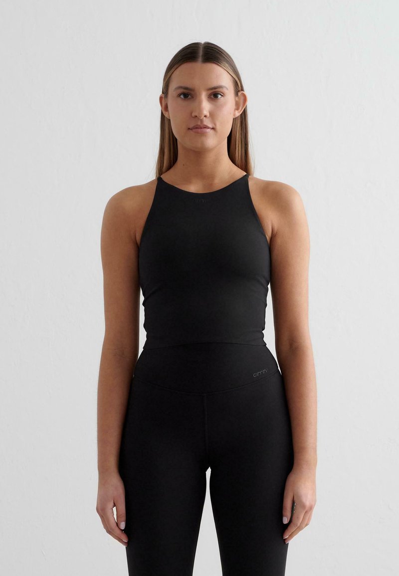 Črn športni top z okroglim izrezom in športnim hrbtom, narejen iz gladkega, raztegljivega materiala. Združen z visokim črnim leggingom.