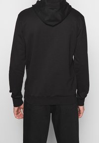 Felpa nera con cappuccio e maniche lunghe, caratterizzata da un design semplice e una texture morbida. Orlo e polsini sono elasticizzati senza motivi visibili.