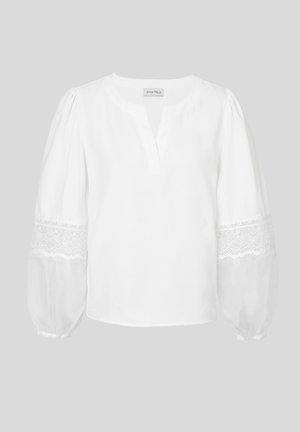 Fehér blúz V-nyakkal, hosszú puffos ujjakkal. A csipke díszítés az ujjvégén textúrát és vizuális érdeklődést ad. Simává szőtt anyag.