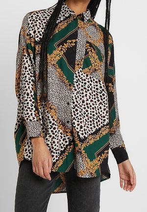 Camicia button-up a vestibilità ampia con stampa animale mista e barocca nei toni del verde, nero, bianco e oro, indossata con pantaloni neri.