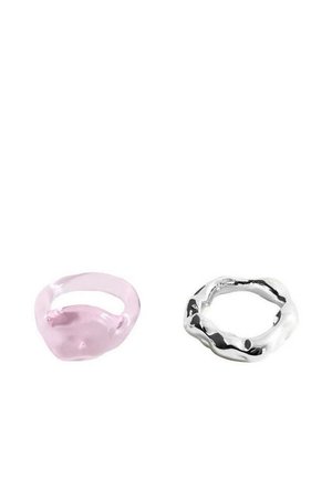 Deux anneaux sur un fond blanc, l’un rose translucide avec des courbes douces, l’autre argenté métallique avec une forme ondulée irrégulière.