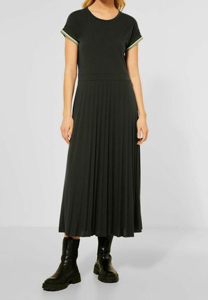 Černé plisované maxi šaty s kulatým výstřihem a krátkými rukávy s zelenými akcenty, vyrobené z měkké tkaniny, doplněné černými masivními botami.