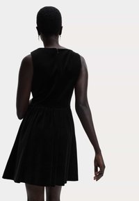 Černé bezramínkové šaty s přiléhavým tělem a rozšířenou sukní, s jemným zipem na zádech. Hladká textura látky.