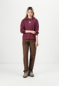 Vinröd huvtröja med en liten logotyp, kombinerad med bruna byxor och beige ankelstövlar. Slät tyg, avslappnad passform och dragsko-detaljer.