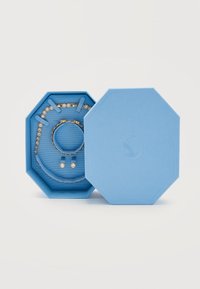 Μπλε οκτάγωνο κουτί κοσμημάτων που περιέχει ένα χρυσό και διαμαντένιο βραχιόλι, κολιέ και ζευγάρι σκουλαρίκια καρφίτσες σε λευκό φόντο.