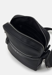 Black leather crossbody bag with a textured finish, zip closure, and interior compartments. Features a silver hardware accent and logo.