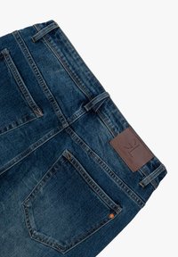 Jeans dżinsowe w ciemnoniebieskim kolorze, z skórzaną naszywką, pięcioma kieszeniami i kontrastowym szwem. Materiał jest teksturowany, z delikatnym wyblaknięciem.