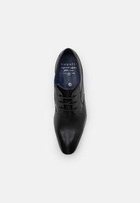 Chaussure habillée en cuir noir avec un bout pointu, présentant une texture lisse et six œillets pour les lacets. L'intérieur a une touche de bleu et un logo.