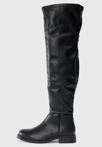 Botas negras hasta la rodilla de cuero suave, con punta redonda, tacón bajo y un caña ligeramente holgada con detalles de costura.