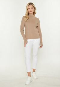 Beige gerippter Rollkragenpullover mit langen Ärmeln, kombiniert mit weißen Skinny Jeans und weißen Sneakern. Glatte Textur, enganliegendes Design.